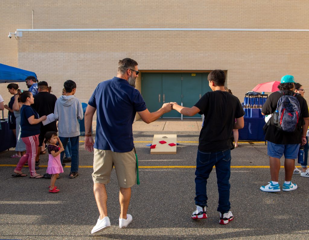 A Kennedy teacher and student fist bump after they play a round of cornhole at Back to School Night.